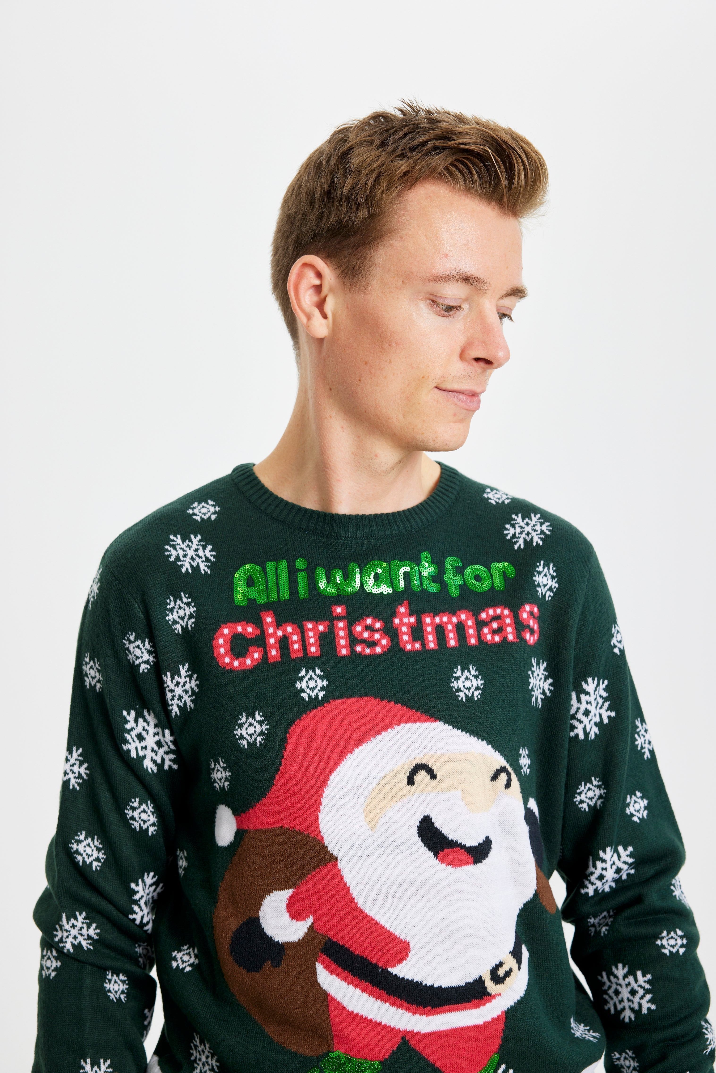 Un homme souriant portant un pull de Noël vert et blanc avec la citation